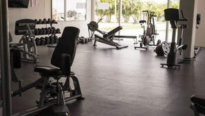 Une salle de sport équipée de divers appareils d’exercice, notamment des haltères, un banc de développé couché et des appareils de cardio.
