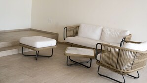 Un salon moderne avec un canapé blanc, deux fauteuils assortis et un petit pouf.