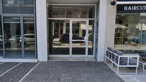 A building entrance with glass doors, a bench outside, and a sign for a hair salon visible through the glass. - Bijou apartment in Glyfada center (Glyfada)