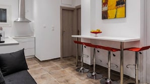 A modern kitchen with a white countertop, a stainless steel range hood, and a red bar stool. - Bijou apartment in Glyfada center (Glyfada)