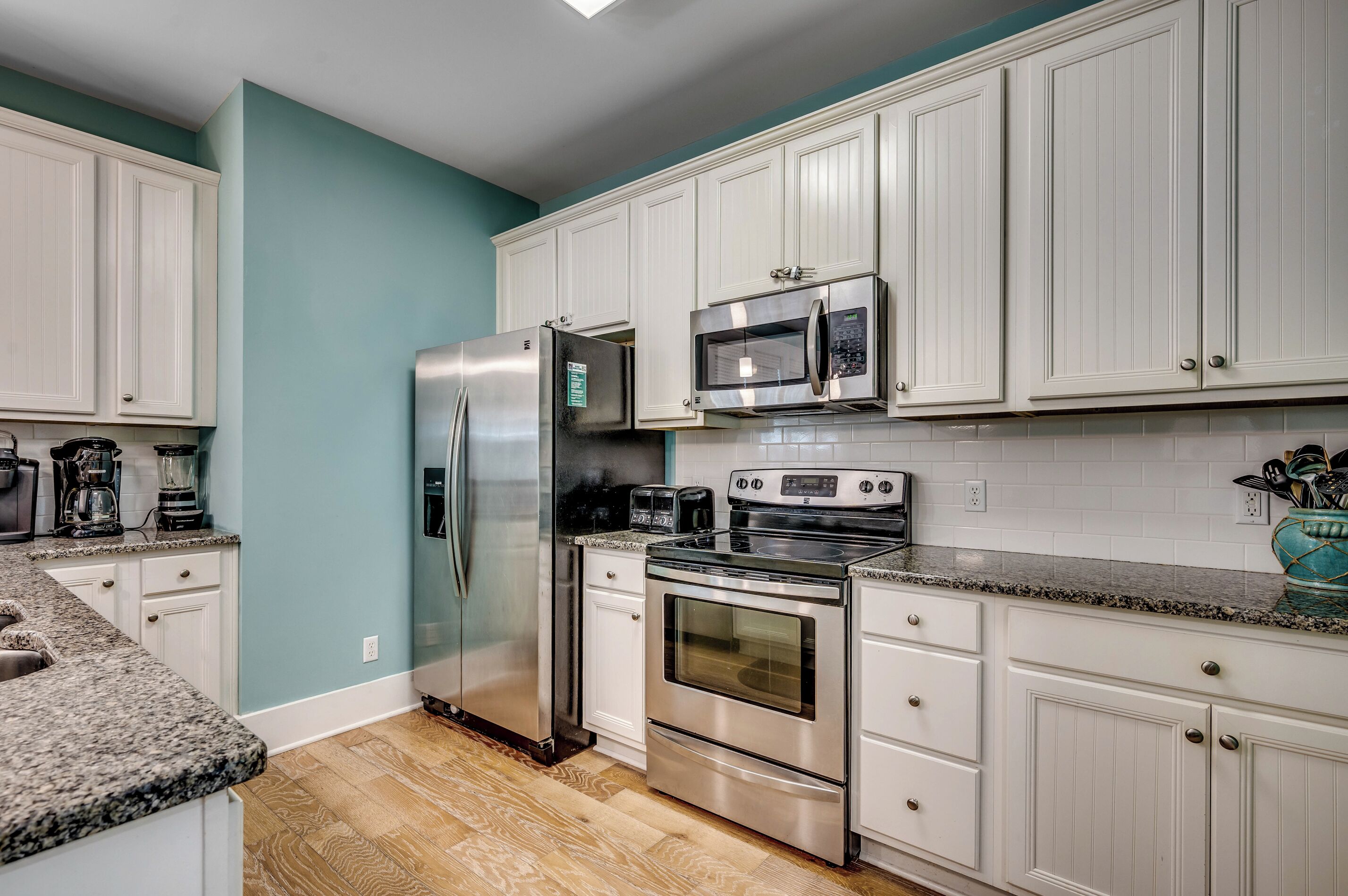 A modern kitchen with white cabinets, stainless steel appliances, and a teal accent wall.