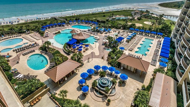 A resort with multiple swimming pools, sun loungers, and a beach view.