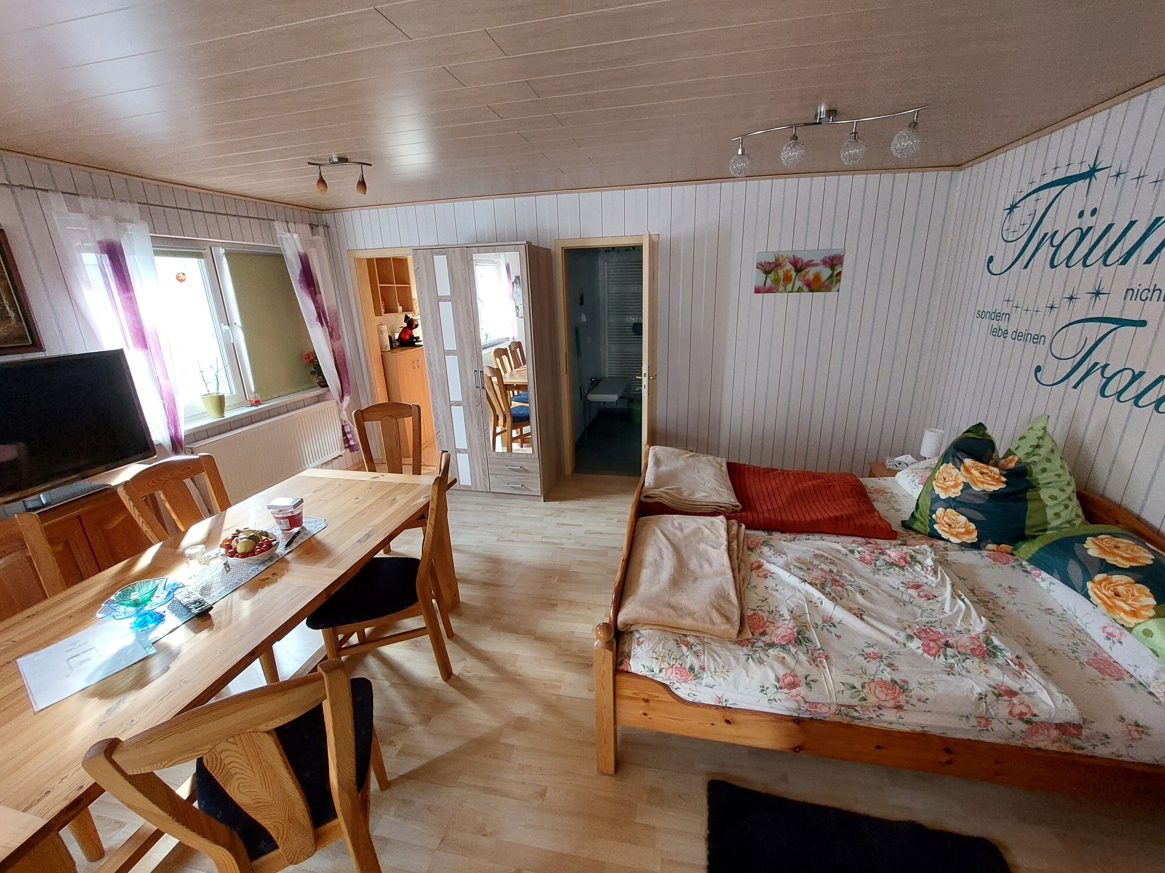 Een gezellige kamer met een houten eettafel, stoelen, een bed met bloemenbeddengoed en een televisie.