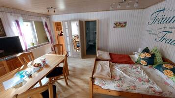 Een gezellige kamer met een houten eettafel, stoelen, een bed met bloemenbeddengoed en een televisie.