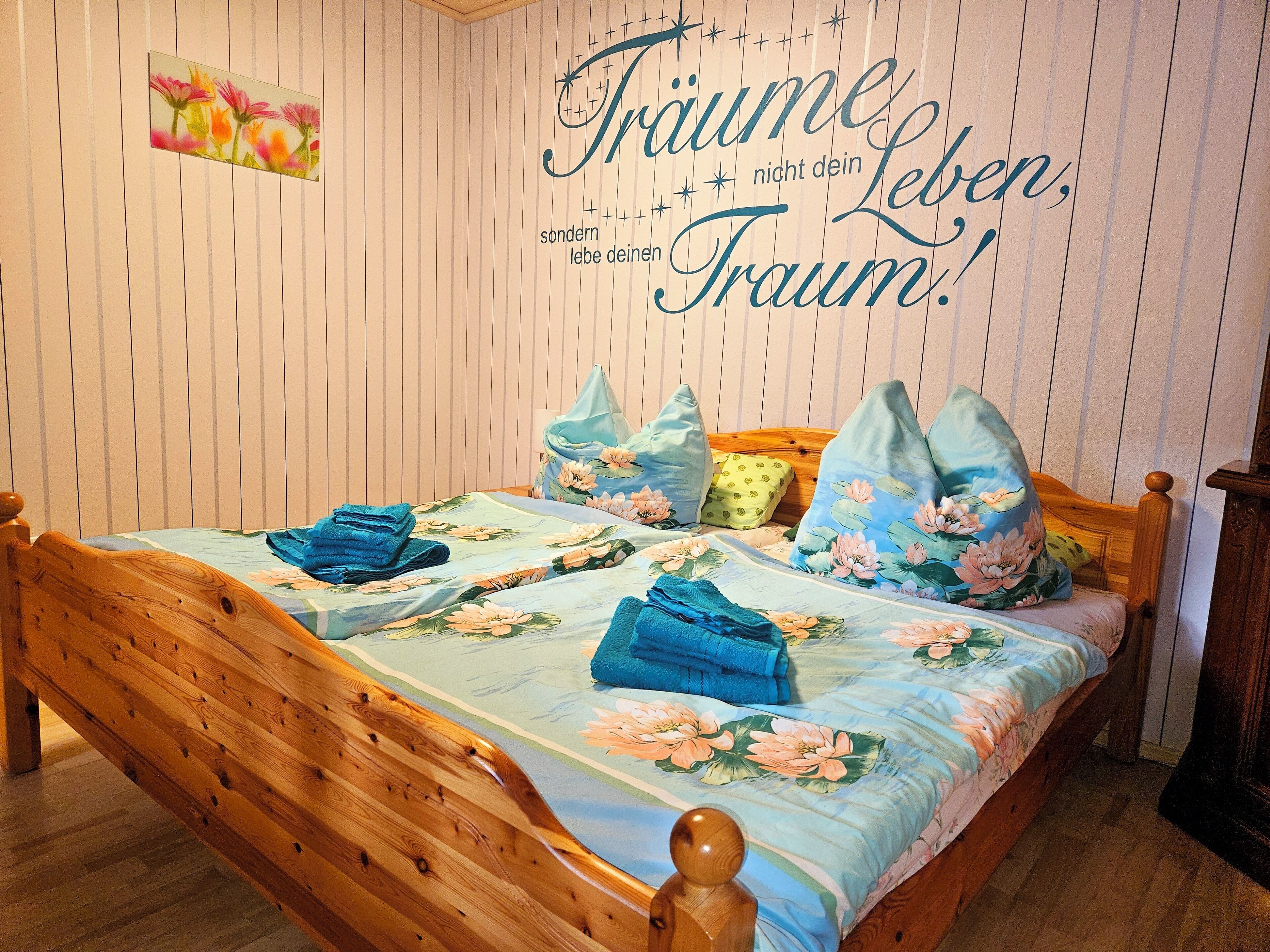 Un dormitorio con cama de madera, ropa de cama floral y una pared con una frase decorativa.