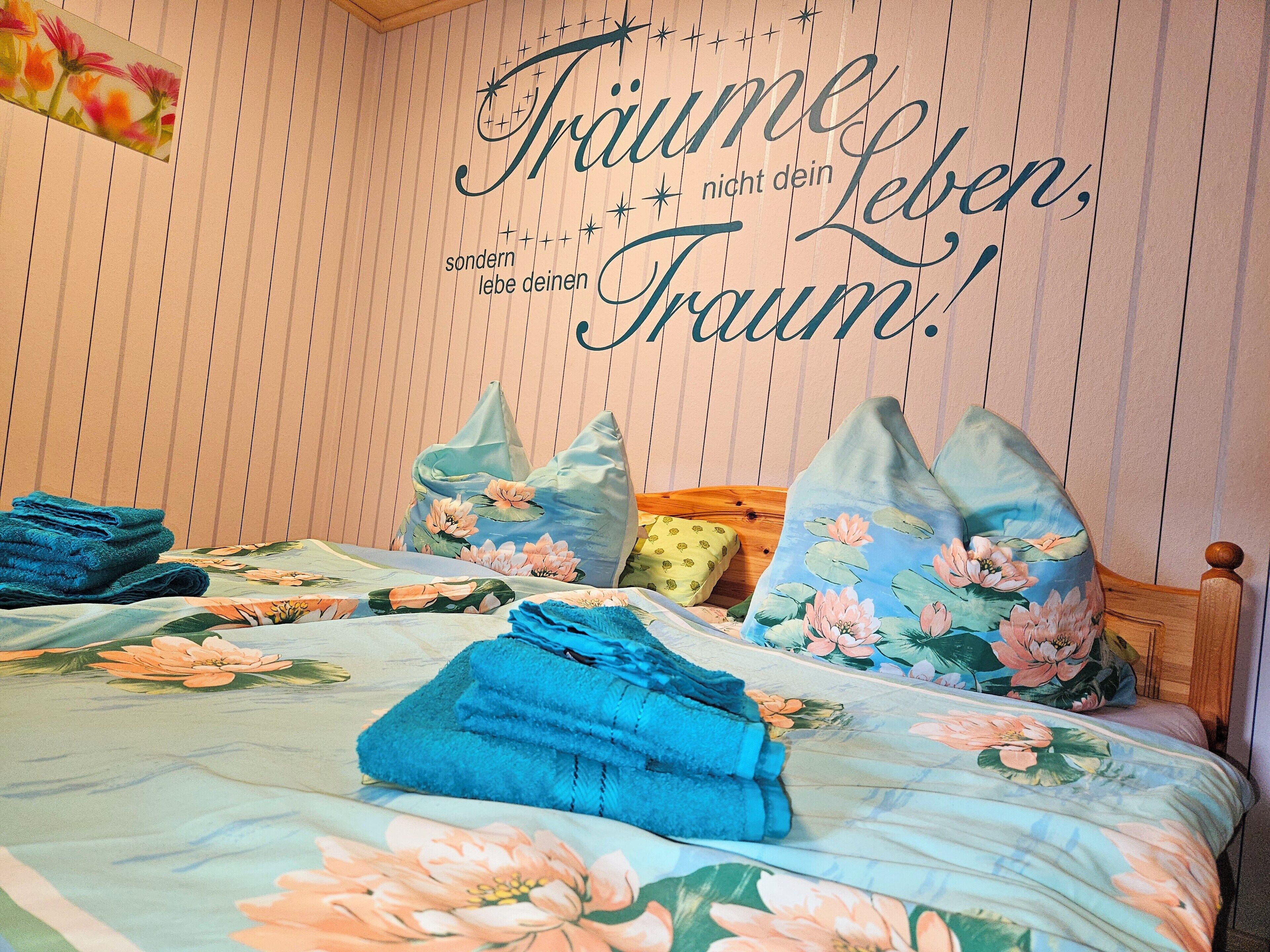 Ein ordentlich bezogenes Bett mit Blumenmuster, Kissen und gefalteten Handtüchern.