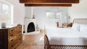 A bedroom with a wooden bed, a dresser, a fireplace, and a window. - Encanto Saguaro | Chic Adobe Home w/ Private Courtyard on 1.5 Acres (Cave Creek)