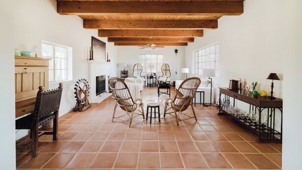A spacious room with a high ceiling, wooden beams, a dining area with chairs and a table, and a side table with glassware. - Encanto Saguaro | Chic Adobe Home w/ Private Courtyard on 1.5 Acres (Cave Creek)