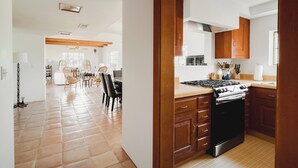 A modern kitchen with wooden cabinets, a stove, and a dining area with chairs and a table. - Encanto Saguaro | Chic Adobe Home w/ Private Courtyard on 1.5 Acres (Cave Creek)