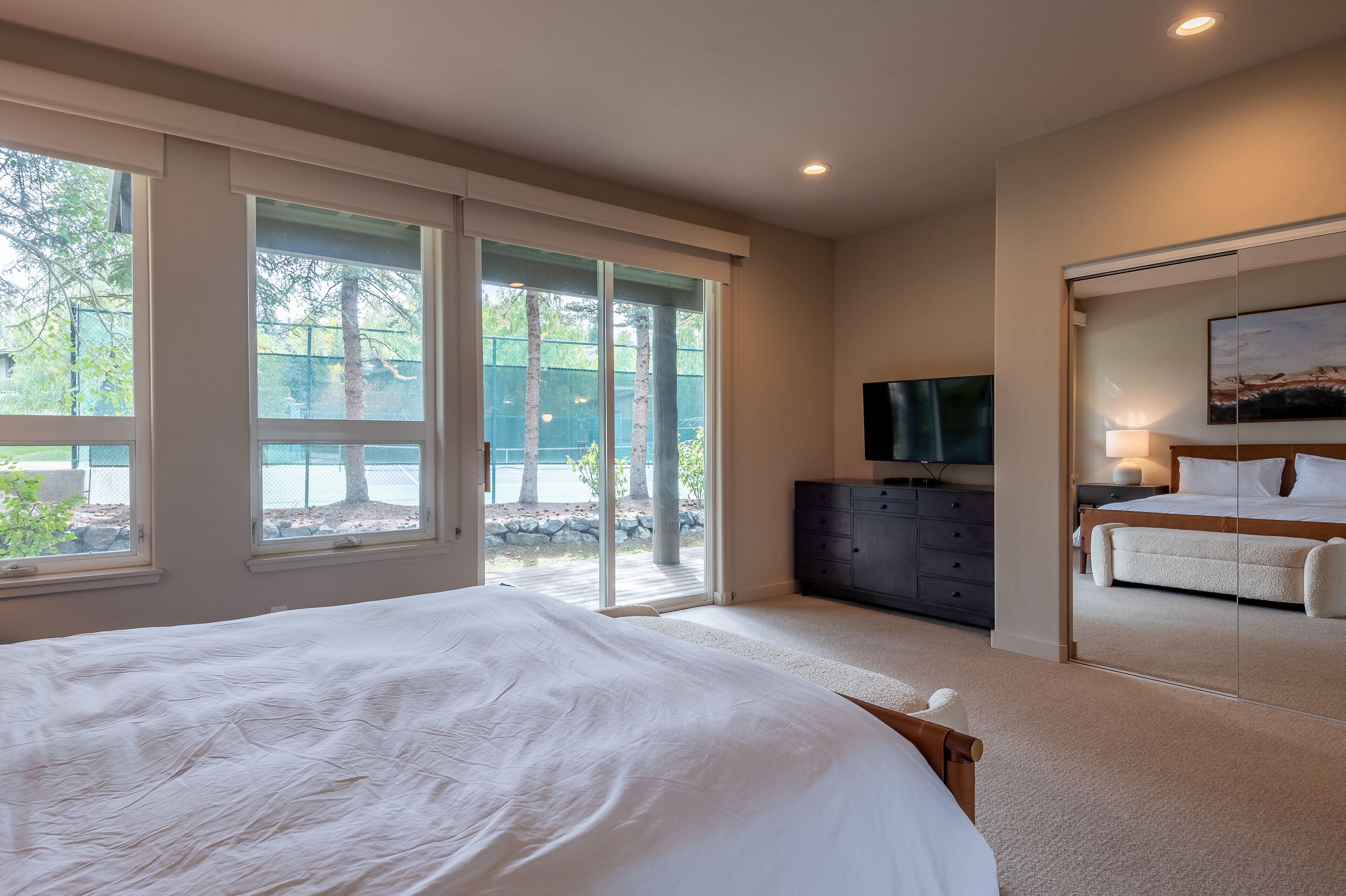 A bedroom with a large bed, a dresser, a TV, and a sliding glass door leading to a balcony.