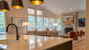 A modern kitchen with a large island, a stone fireplace, and a seating area with a sofa and chairs.