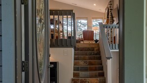 A staircase with stone steps leading to a second floor, a door with a glass panel, and a view of a room with a chair and lamp.