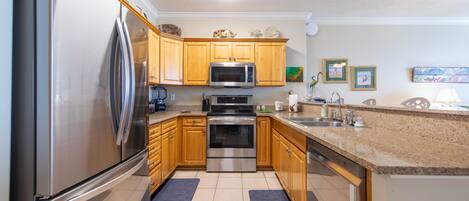 A modern kitchen with stainless steel appliances, wooden cabinets, granite countertops, and a tiled floor.