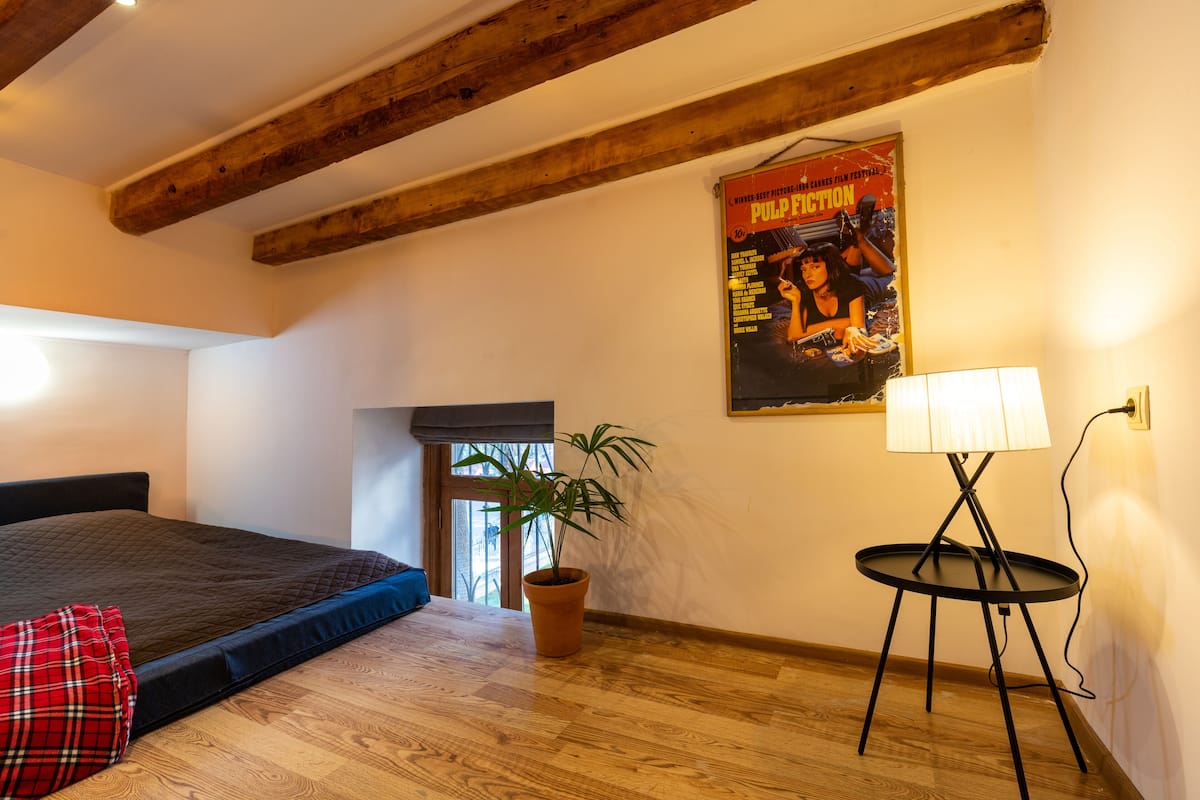 A bedroom with a bed, a potted plant, a lamp, and a poster on the wall.