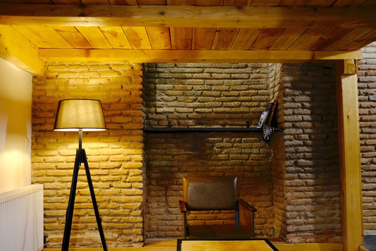 A room with a brick wall, a wooden ceiling, a floor lamp, and a chair.