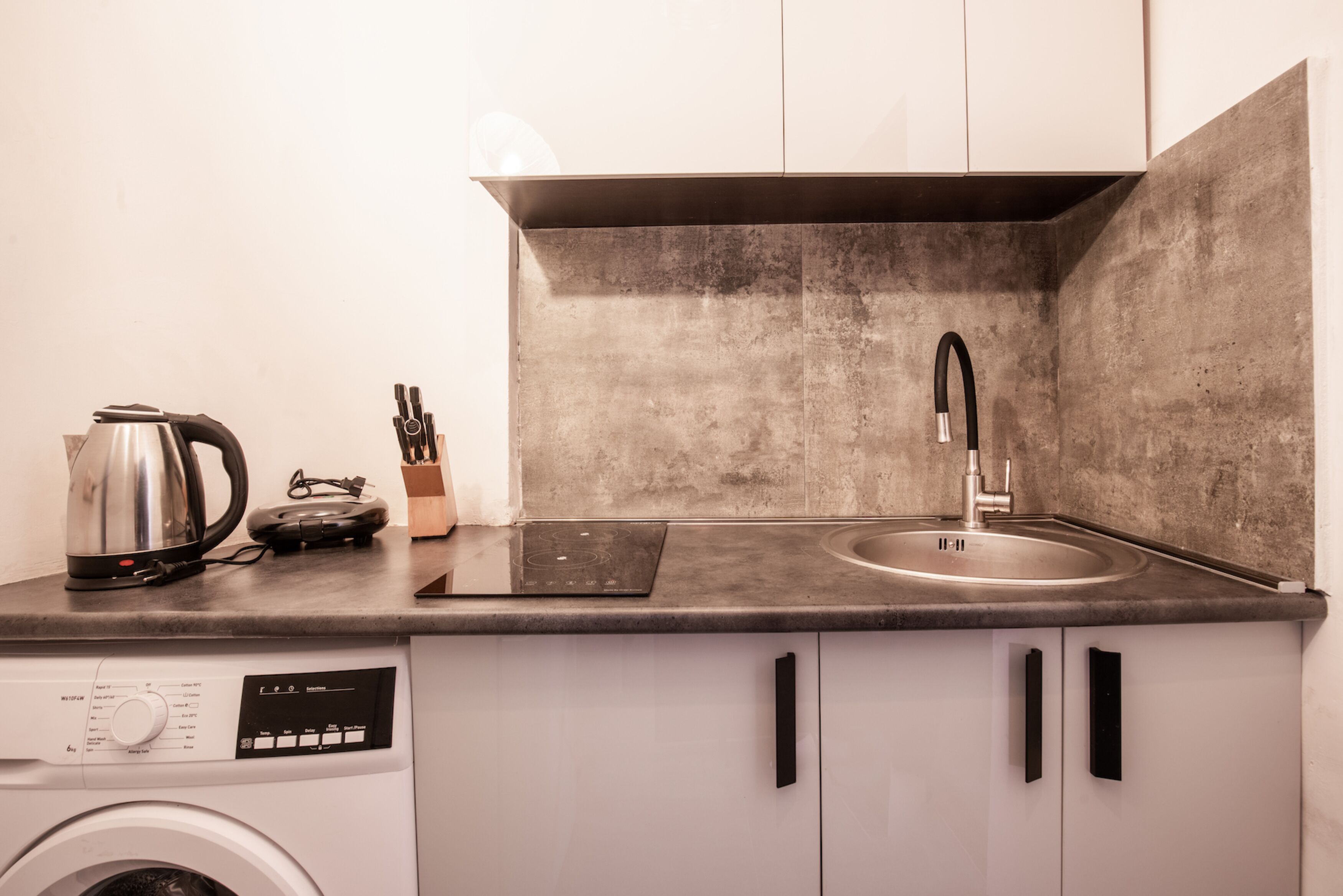 A compact kitchen with a washing machine, a kettle, and a sink.
