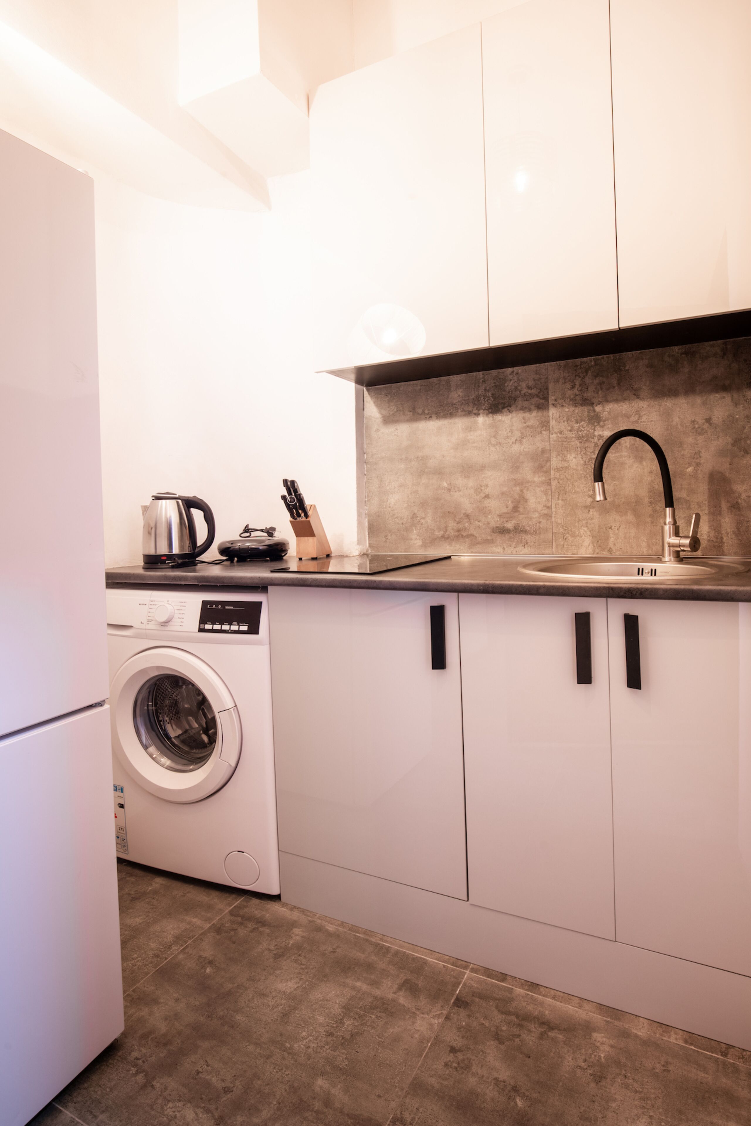 Een kleine keuken met een wasmachine, een spoelbak en een aanrecht met waterkoker en messen.