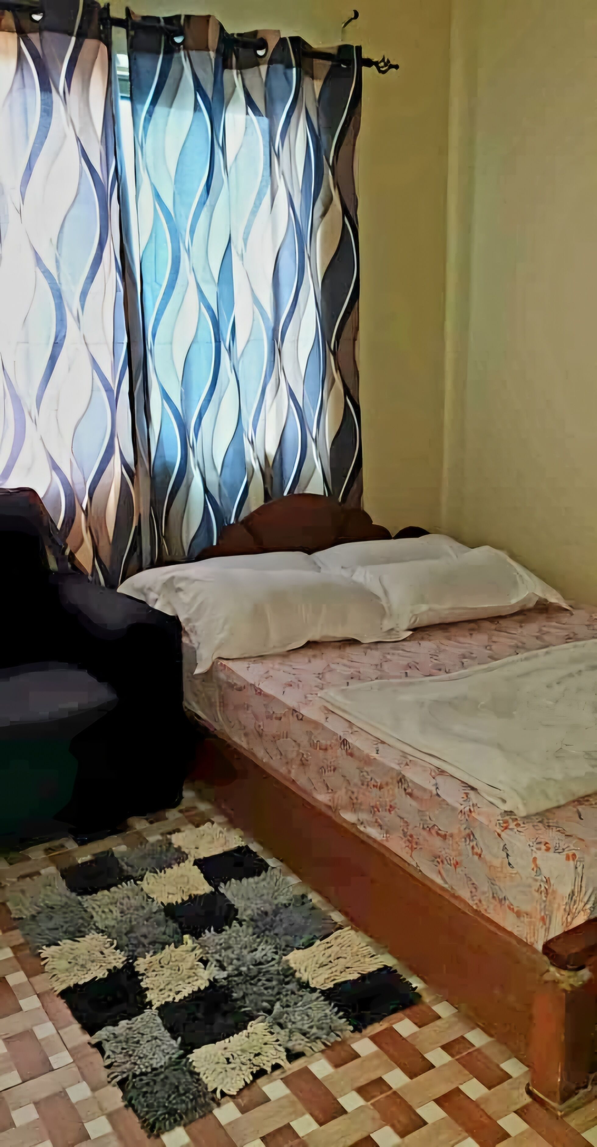 Een slaapkamer met een bed, een kamerkleed met patroon en gordijnen.