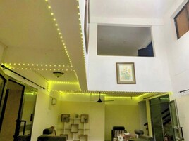 Sala de estar com ventoinha no teto, sofá e uma pequena mesa. Há um quadro na parede e uma janela com vista para o exterior.