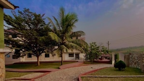 Un sendero pavimentado que conduce a un edificio de techo rojo, rodeado de follaje y un cielo despejado.
