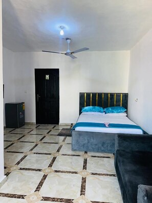 A bedroom with a bed, a ceiling fan, a door, and a tiled floor.