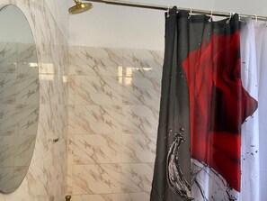 A bathroom with marble tiles, a shower with a black and red curtain, and a gold showerhead.