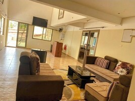 Um hall amplo com um sofá, poltronas e uma mesa de centro. Há um extintor de incêndio e uma porta que dá para o exterior.