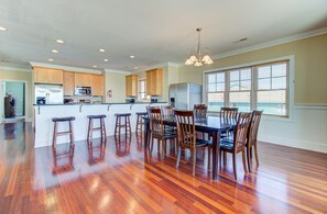 A spacious kitchen with wooden cabinets, a central island with stools, and a dining table with chairs. - 🏖️Ocean Overlook-Beautiful 6BR Oceanfront Top 2 Floors of a Duplex🏖️ (Carolina Beach)