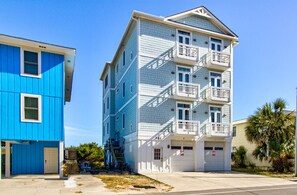 A multi-story building with a light blue exterior and white trim. It has multiple balconies and a garage with a white door. - 🏖️Ocean Overlook-Beautiful 6BR Oceanfront Top 2 Floors of a Duplex🏖️ (Carolina Beach)