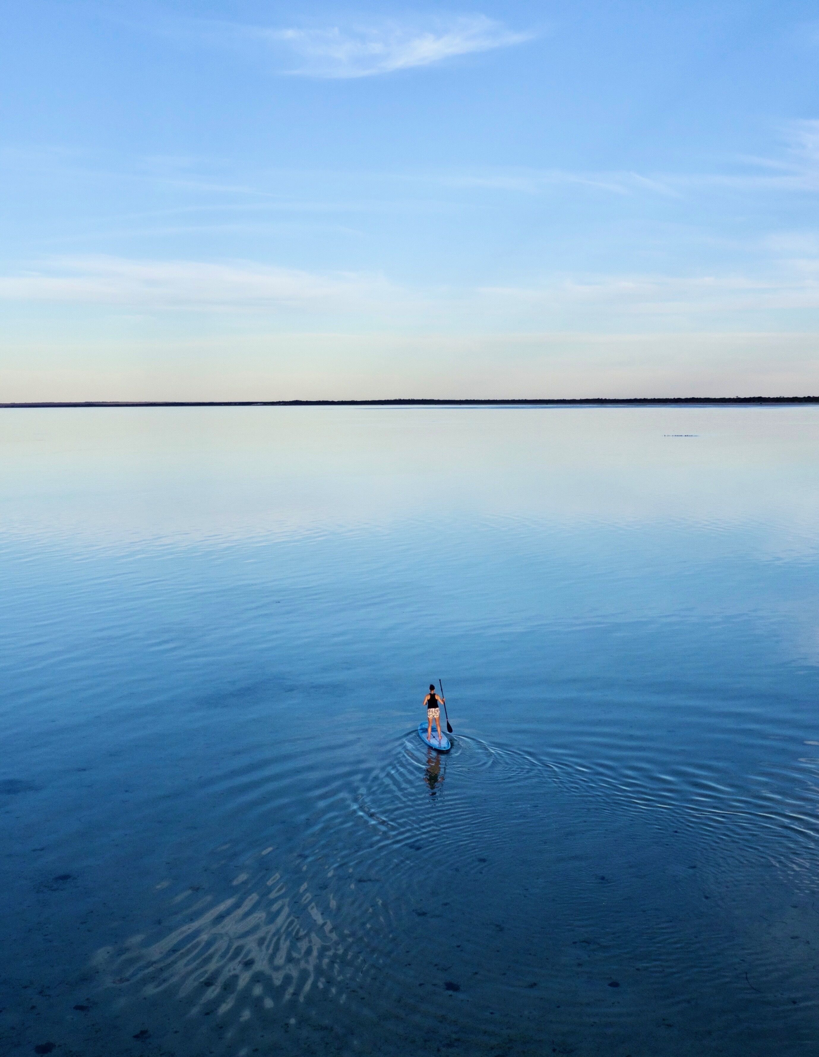 Una persona fent paddle surf sobre un massís d'aigua tranquil·la, sota un cel serè.