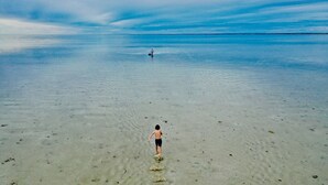 A beach scene with a person walking in shallow water.