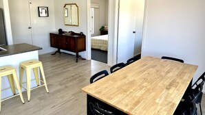 A dining area with a wooden table and black chairs, a kitchen with a built-in stove, and a mirror on the wall.