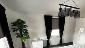 Une chambre moderne avec un grand lit, une commode blanche, une plante en pot et un luminaire suspendu.