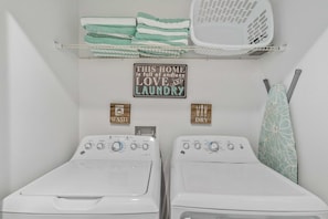 Et vaskerum med to vaskemaskiner, et tørrestativ og et skilt, der står: 'THIS HOME is full of endless LOVE and LAUNDRY'.