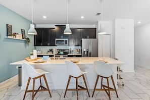 A modern kitchen with dark cabinets, a large island with bar stools, and pendant lighting.