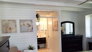 A bedroom with a bed, a dresser, a mirror, and a door leading to a bathroom. - Family friendly condo located in Pineapple Village. (St Thomas)