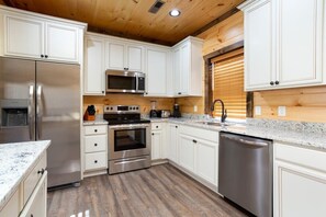 A modern kitchen with white cabinets, stainless steel appliances, and a wooden ceiling.