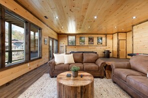 L’intérieur chaleureux d’un chalet avec des murs en bois, de grandes fenêtres, un canapé en cuir marron et une table basse ronde en bois.