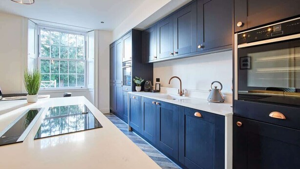 Una cocina moderna con armarios azul oscuro, una encimera blanca y un horno empotrado.