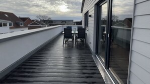 Une terrasse sur le toit, avec une table et des chaises, une porte vitrée et une vue sur les maisons voisines.