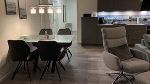 Une cuisine moderne équipée d’un four encastré, d’une machine à café et d’un évier. On y trouve également un coin repas avec une table et des chaises en verre.