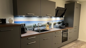 Une cuisine moderne dotée d’un grand îlot central, d’appareils électroménagers en acier inoxydable et d’un revêtement mural décoratif.