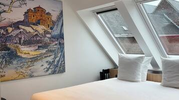Une chambre à coucher avec un grand lit, une lucarne et un tableau représentant un bâtiment.