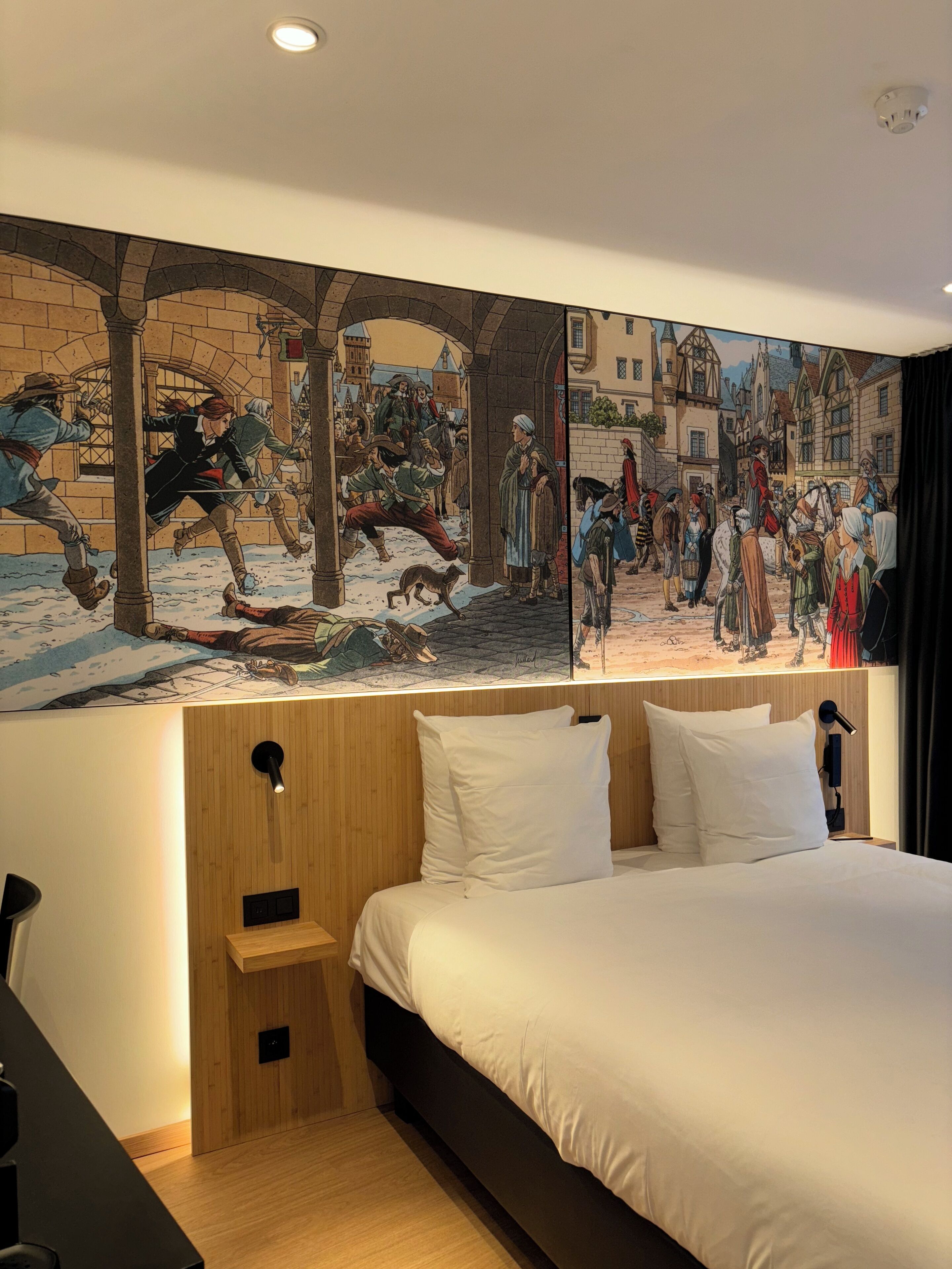 A hotel room with a large mural depicting a historical scene, a wooden headboard, and a bed with white linens.