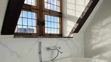 Un baño moderno con una bañera independiente, un ventanal con contraventanas de madera y una pared de mármol.