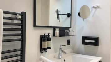 Een moderne badkamer met een witte wastafel, een zwart aanrecht en een grote spiegel. Op het aanrecht staan twee flessen shampoo en conditioner, en een handdoek is opgerold aan de zijkant.