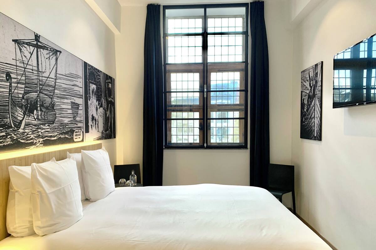 A hotel room with a large bed, a window with curtains, and artwork on the walls.
