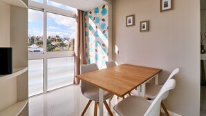 Ein moderner Essbereich mit Holztisch und weißen Stühlen, großen Fenstern mit Blick auf eine Stadtlandschaft und einem dekorativen Vorhang mit Blumenmuster.