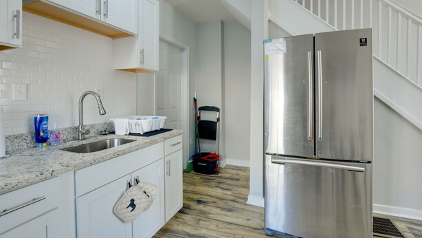 A kitchen with white cabinets, a stainless steel refrigerator, a sink, and a broom in the corner.