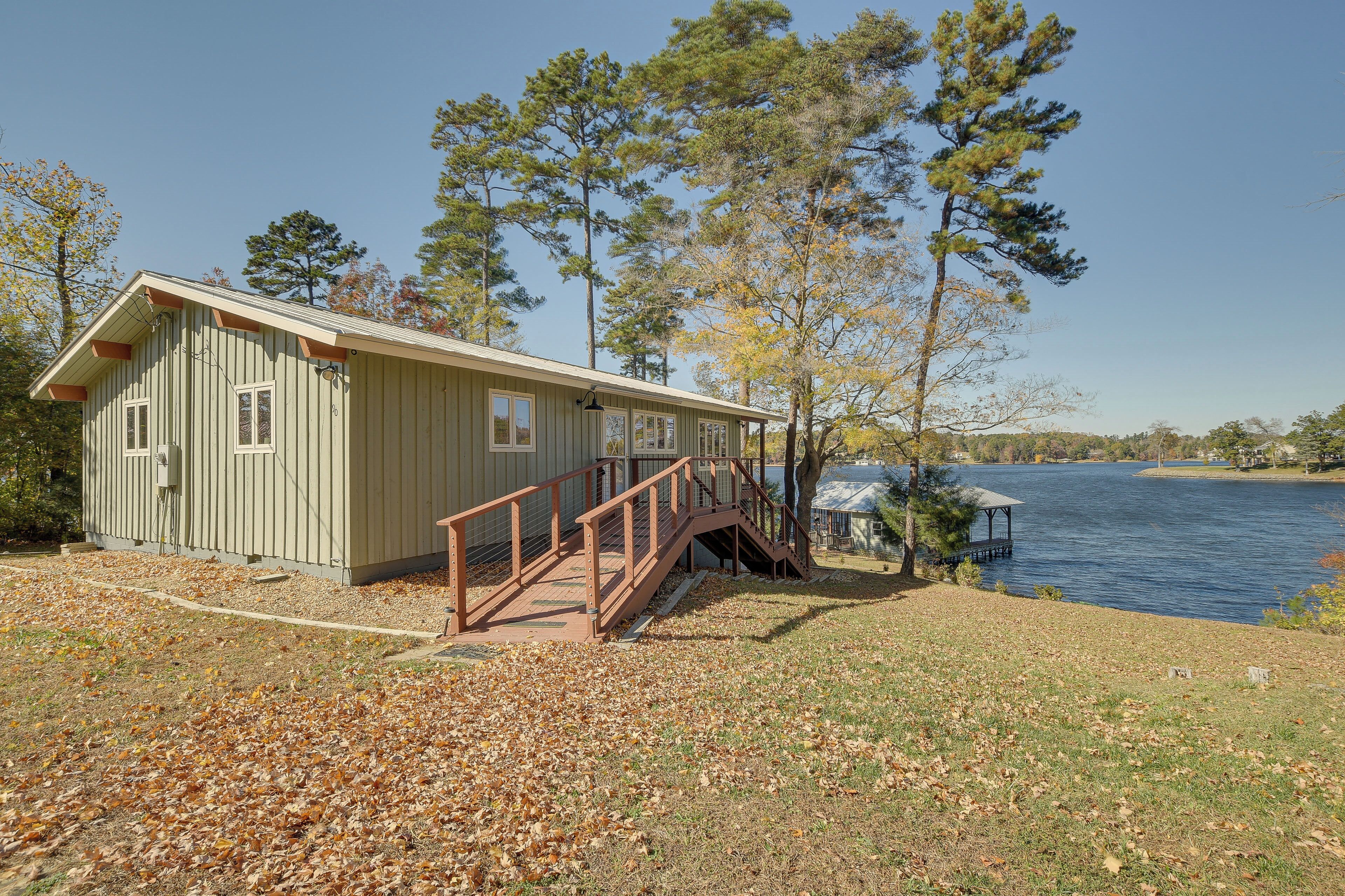 Une cabane au bord d’un lac, avec un quai, un espace abrité et une terrasse en bois.